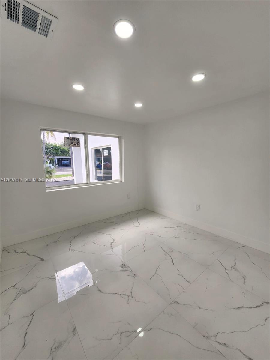 Large-format, light-toned flooring with decorative veining, recessed ceiling lighting, and a single-pane horizontal window