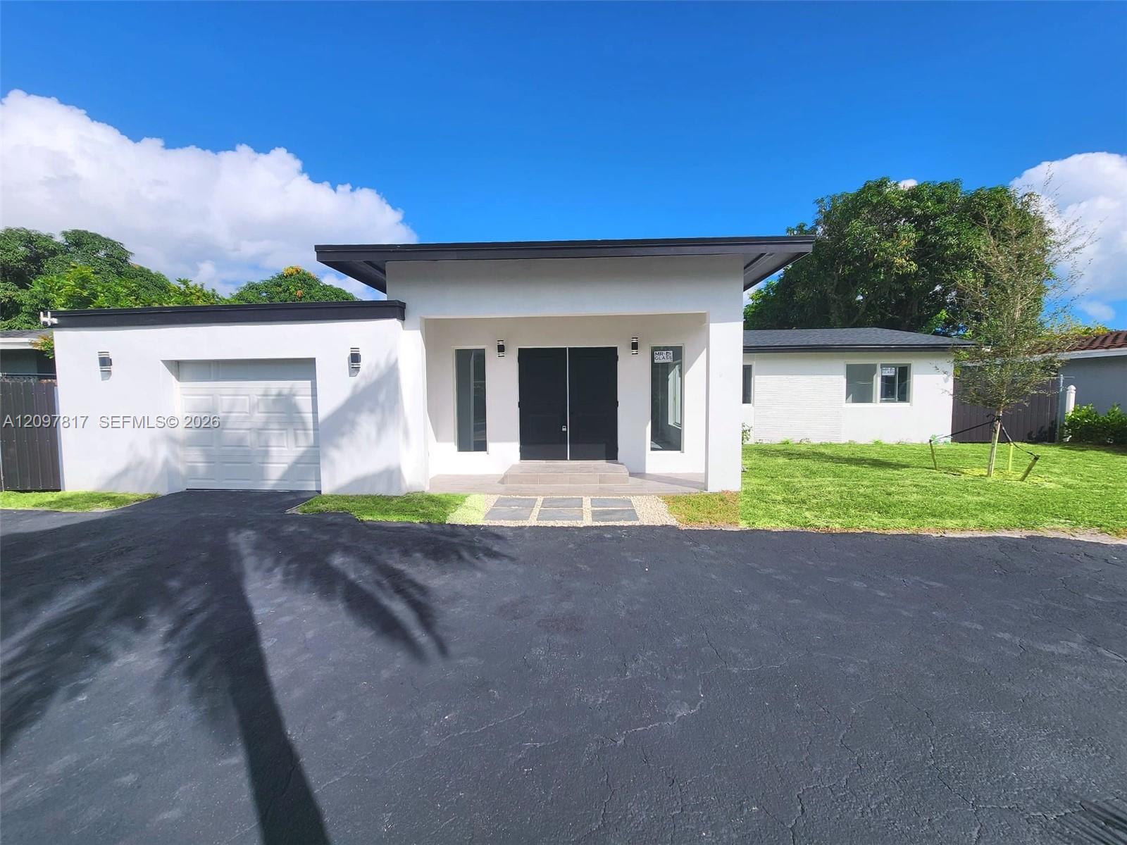 Contemporary single-story exterior featuring a flat roofline, white smooth-finish facade, double-door entryway, attached garage, and a paved driveway