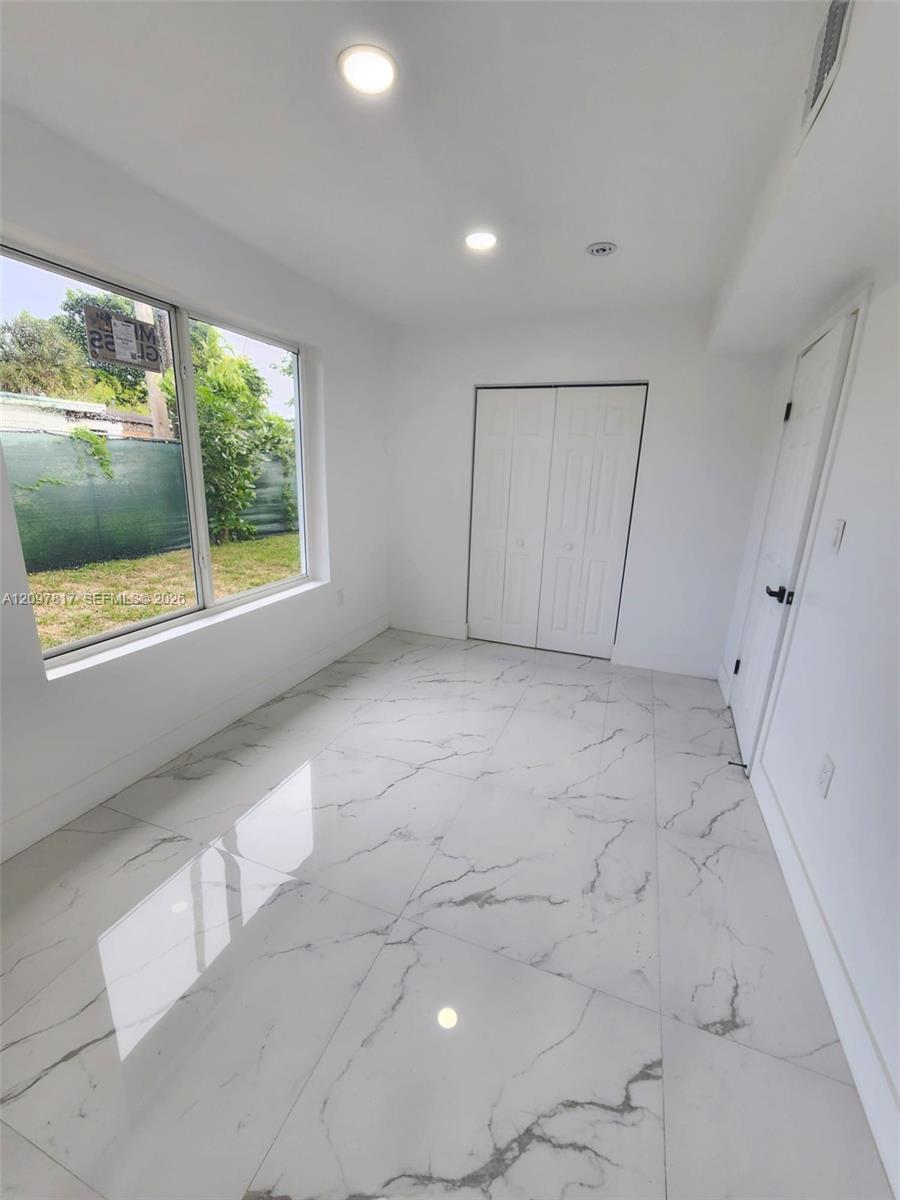 Large-format stone-look tile flooring with veining detail, recessed lighting, and a dual-panel closet door