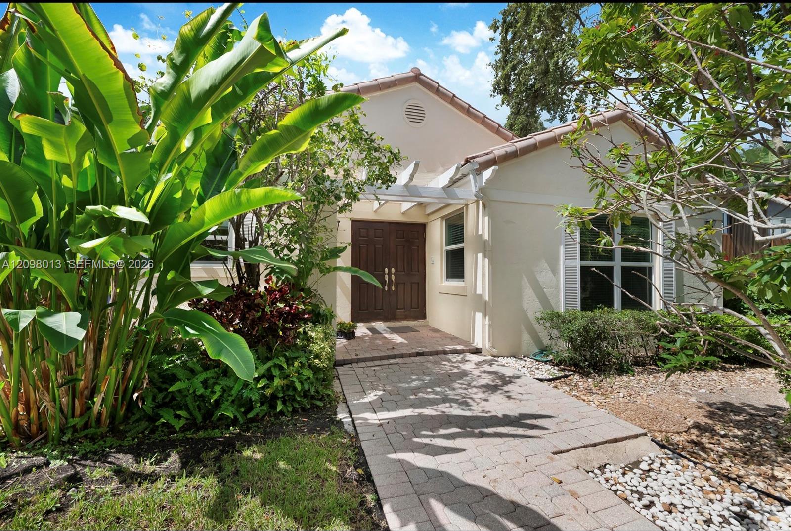 Stucco on concrete exterior featuring a tiled roof, paver stone walkway, double entry doors, and overhead trellis. Built on concrete slab no crawl space.