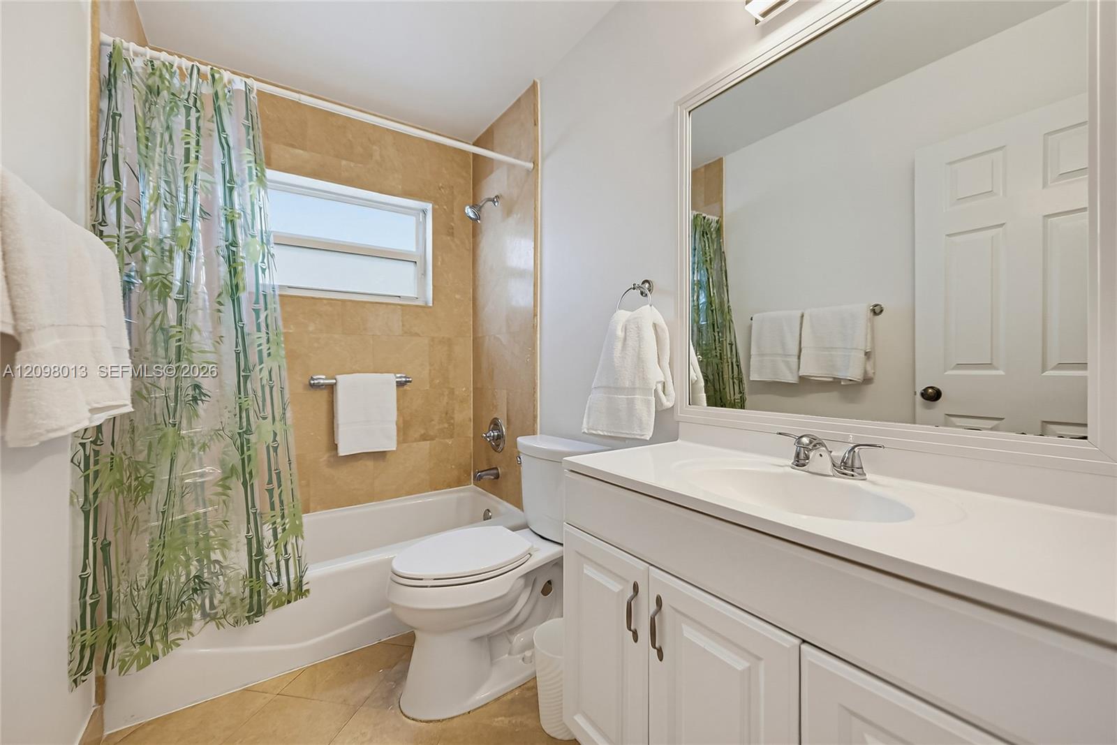 Bathroom featuring a white vanity with an integrated basin, large wall-mounted mirror, tub with natural stone wall