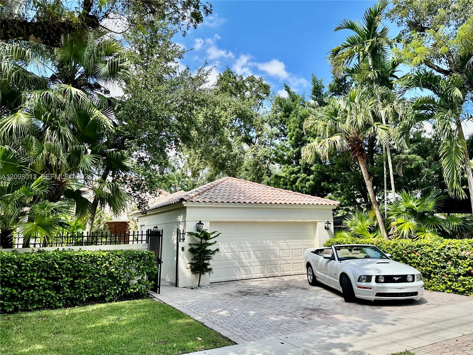 garage featuring a tile roof, stucco exterior, paver driveway, and black metal perimeter fencing surrounded by mature landscaping