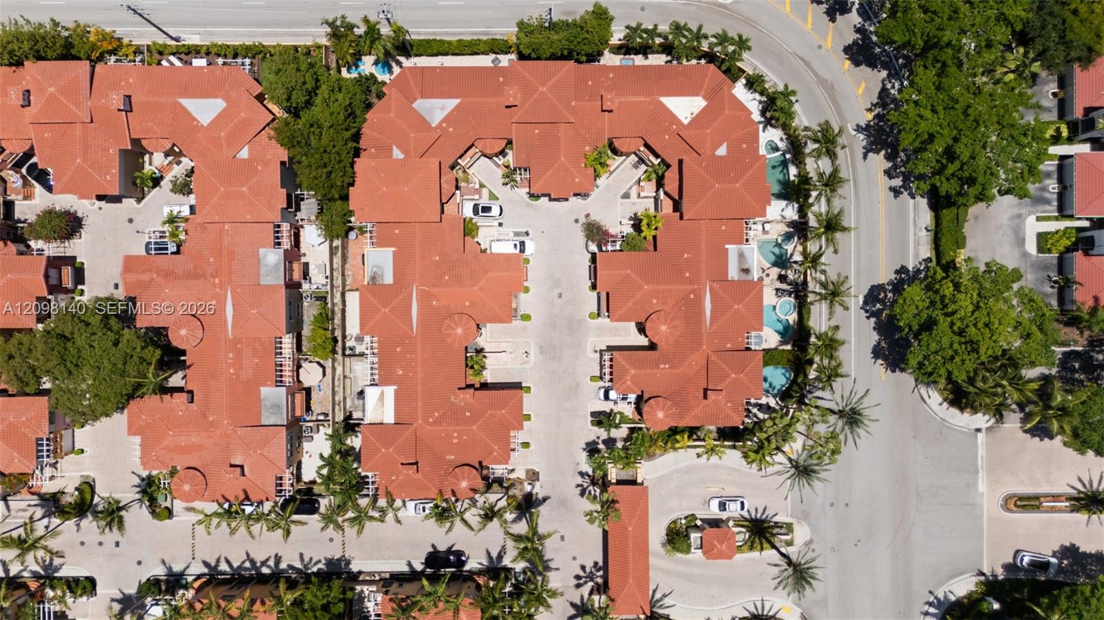 Aerial perspective of a multi-unit complex featuring terra-cotta tile roofing, a paved central parking area, and a swimming pool