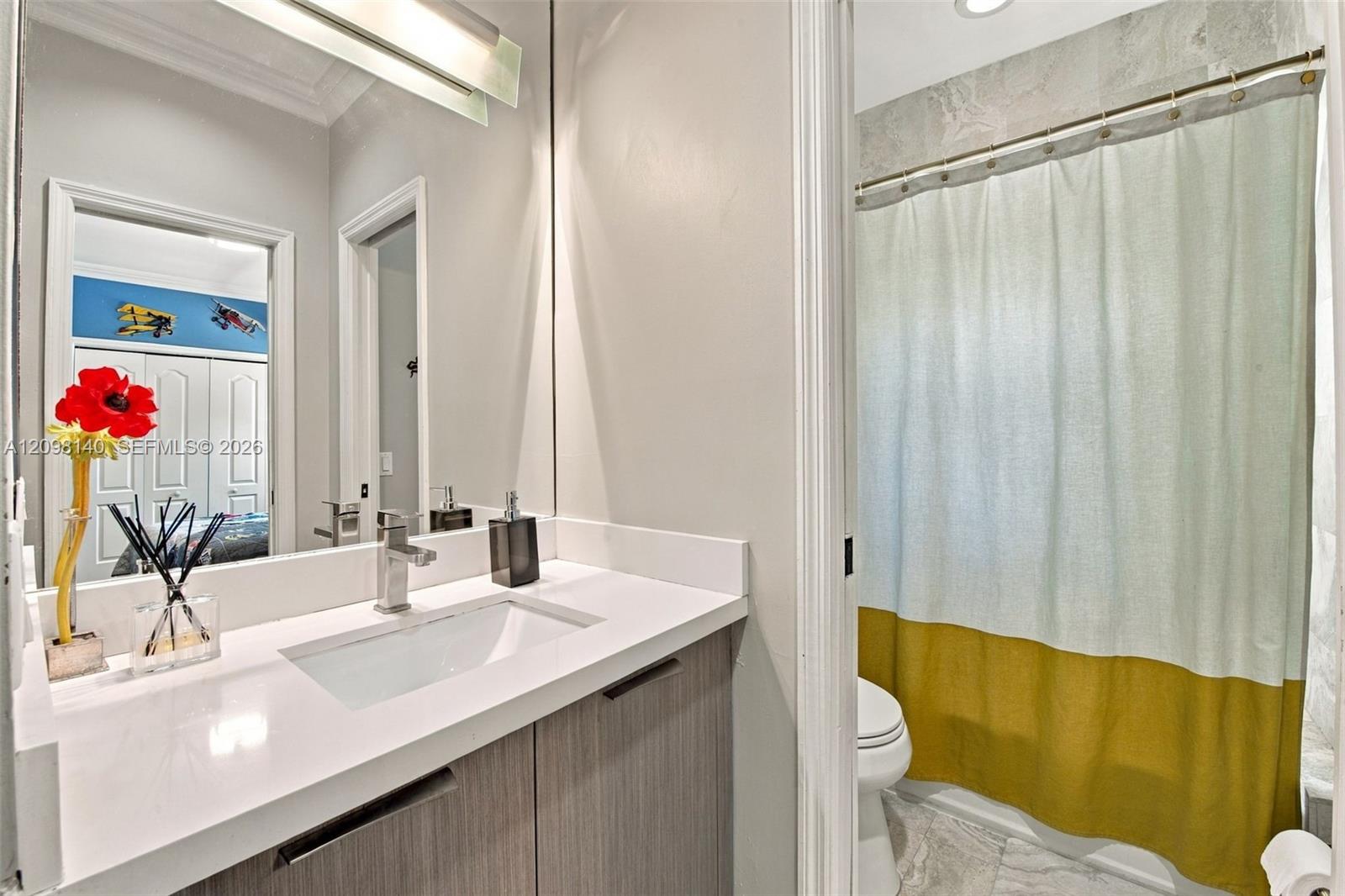 Bathroom vanity with a white countertop, integrated rectangular sink, wood-finish cabinetry, and a full-width mirror with an overhead light fixture
