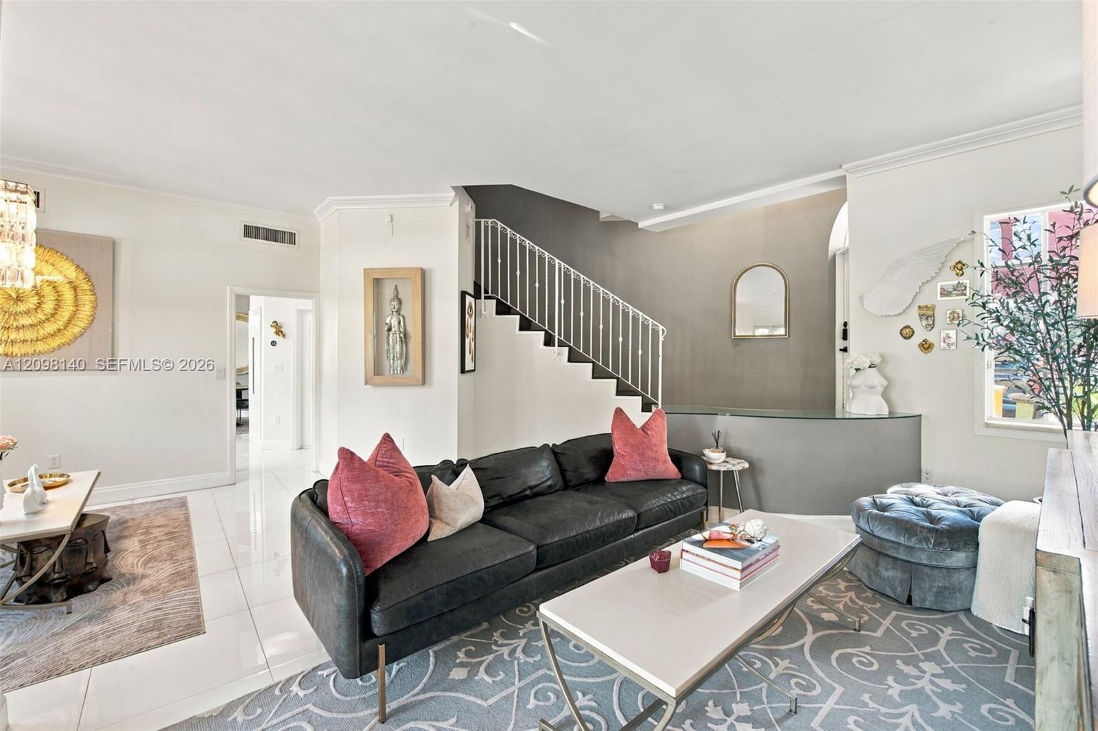 Open-concept interior featuring polished tile flooring, a metal-railed staircase, high ceilings with crown molding, and a curved architectural partition wall