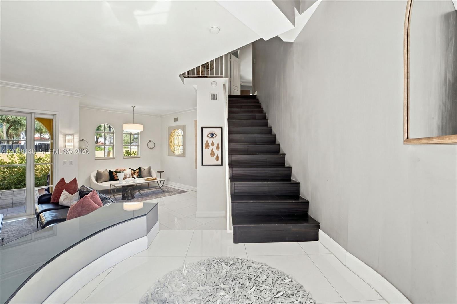 Open floor plan featuring large-format tile flooring, a dark-finish staircase, arched windows, and glass sliding doors