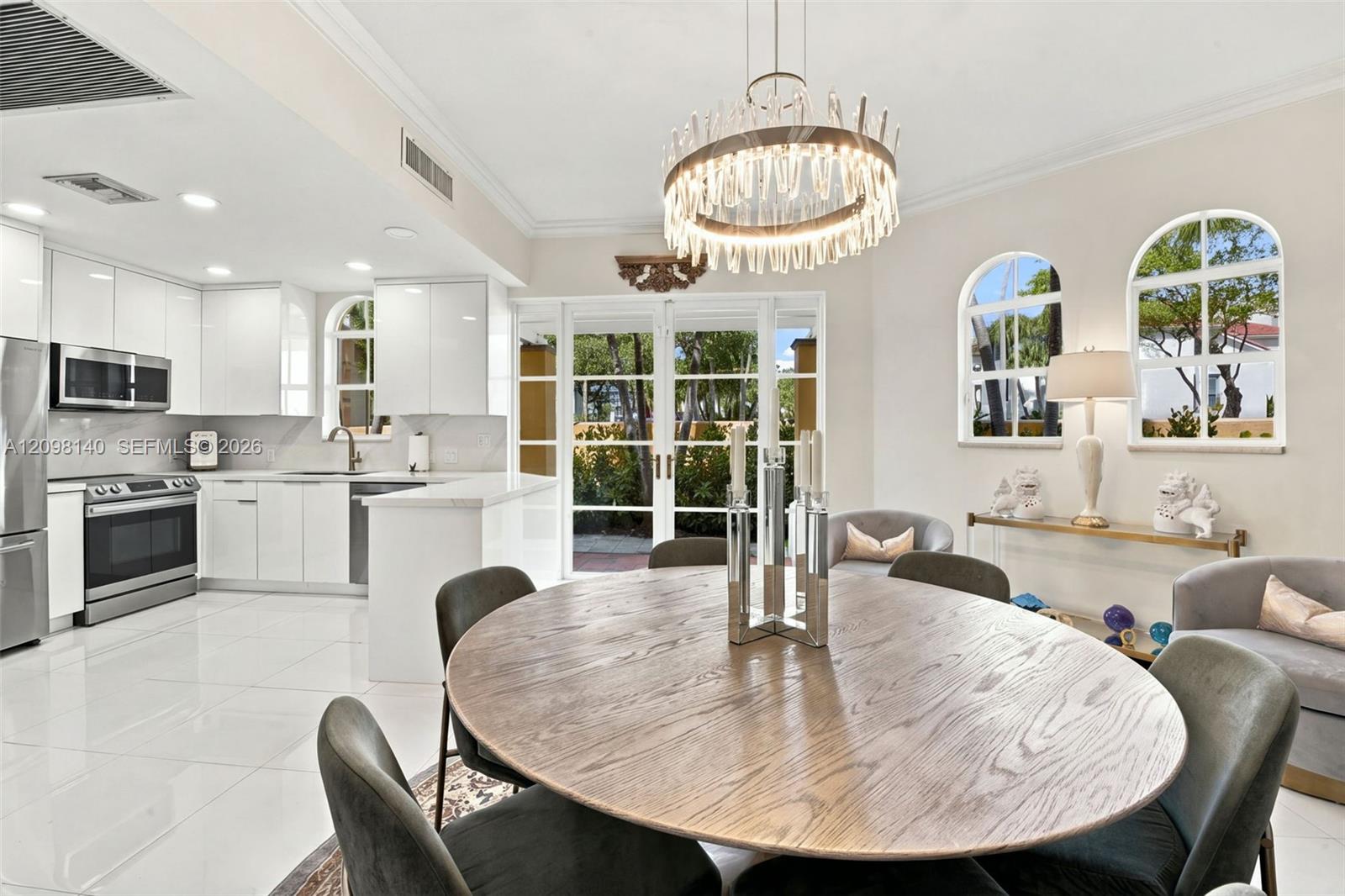 Kitchen and dining area featuring high-gloss cabinetry, stainless steel appliances, polished stone-finish flooring, a contemporary drum chandelier, and arched windows