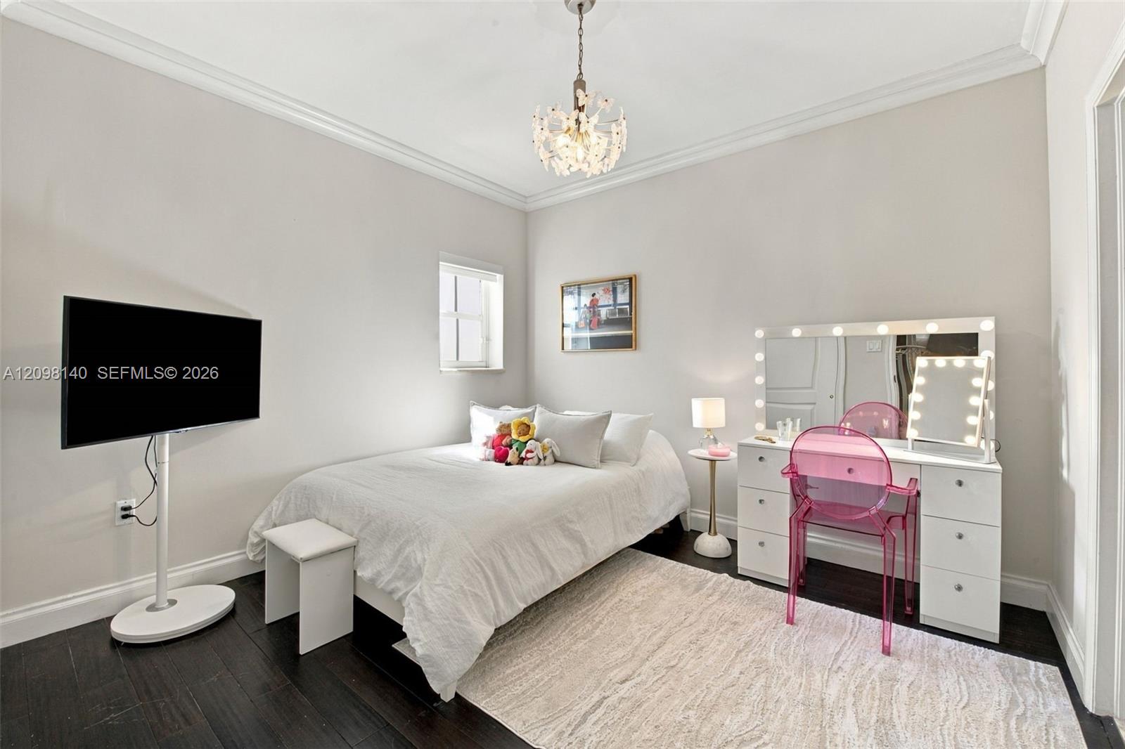 Neutral-toned bedroom featuring dark wood-finish flooring, crown molding, and a tiered crystal chandelier