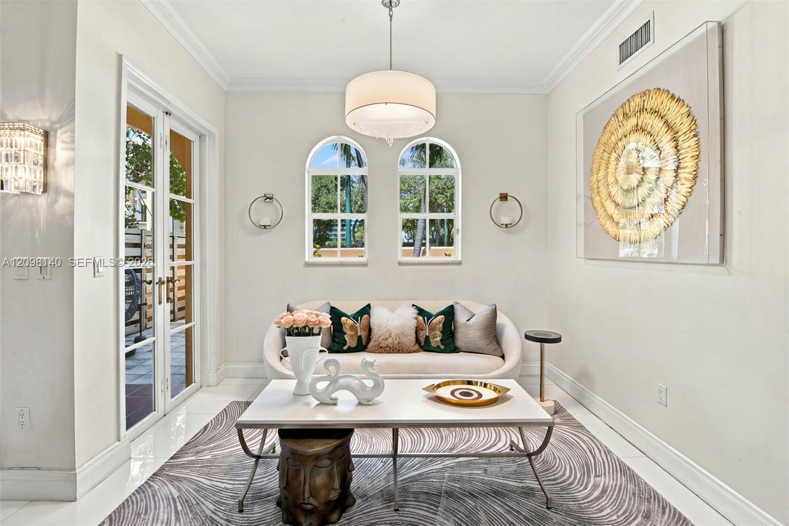 Arched windows with grid panes, glass-paned double doors, crown molding, and a central drum pendant light fixture