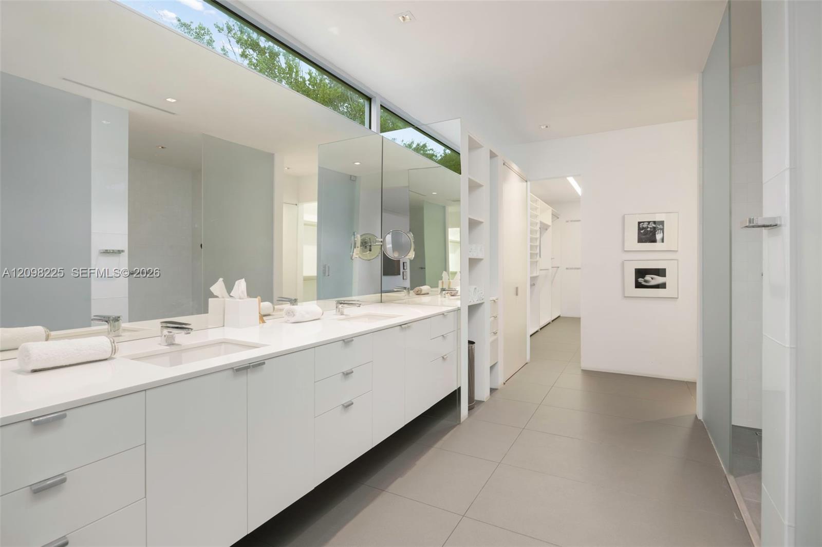 Dual-sink vanity with clean-lined cabinetry, stone-finish countertops, expansive horizontal mirror, transom window, and large-format tile flooring