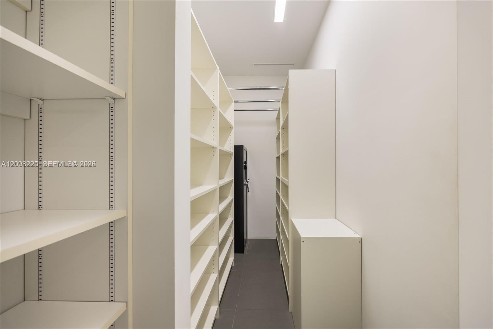 Floor-to-ceiling built-in white shelving, adjustable shelving hardware, overhead recessed lighting, and large-format tile flooring