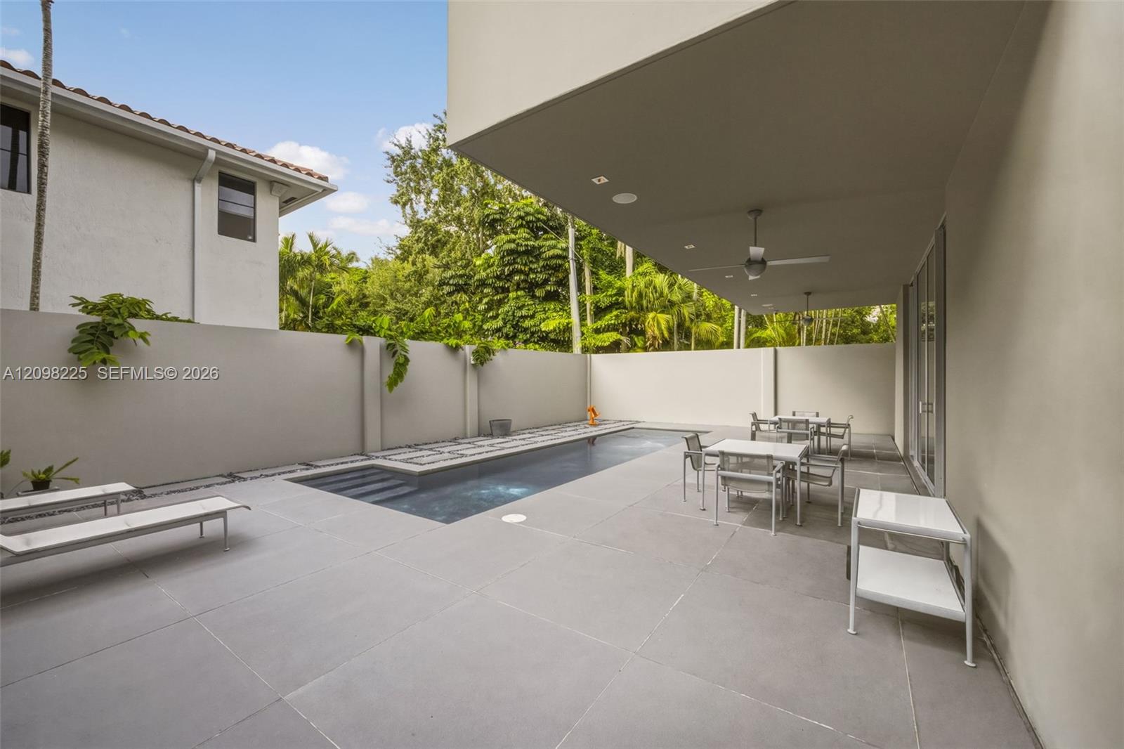 Covered patio featuring recessed ceiling lighting, ceiling fans, large-format stone pavers, a rectangular swimming pool, and a perimeter privacy wall