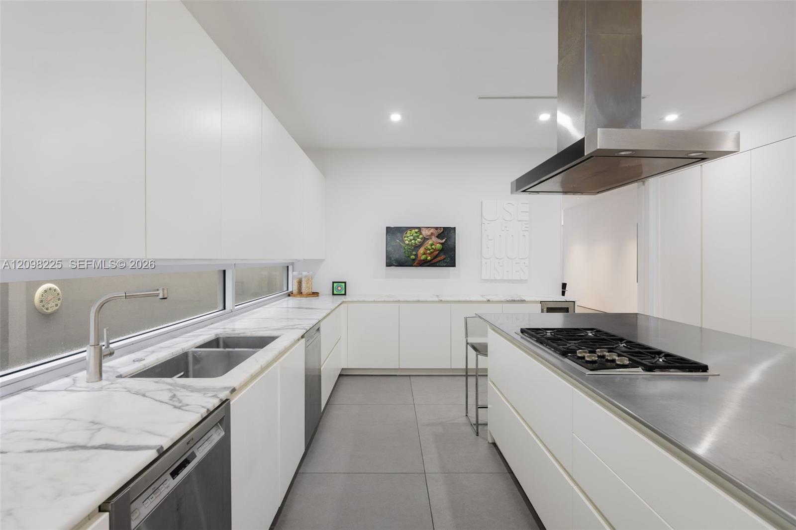 Contemporary kitchen featuring flat-panel cabinetry, stone countertops, stainless steel island cooktop with hood, and large-format tile flooring