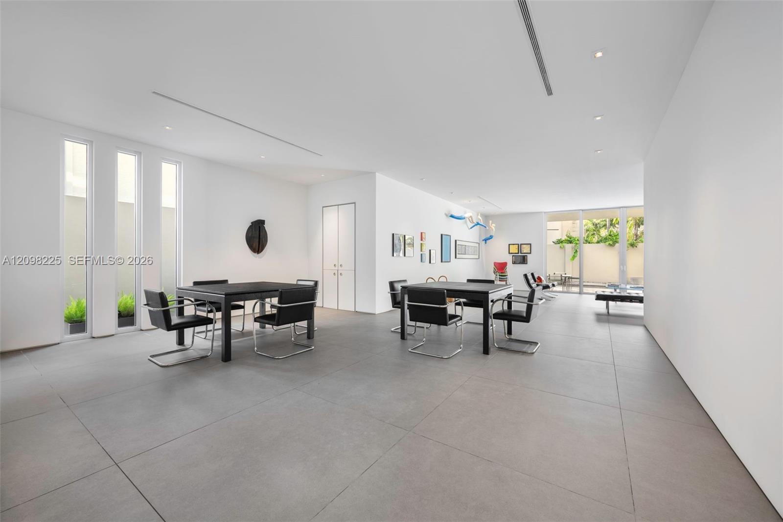 Expansive open-concept room featuring large-format tile flooring, recessed linear lighting, floor-to-ceiling windows, and glass sliding doors