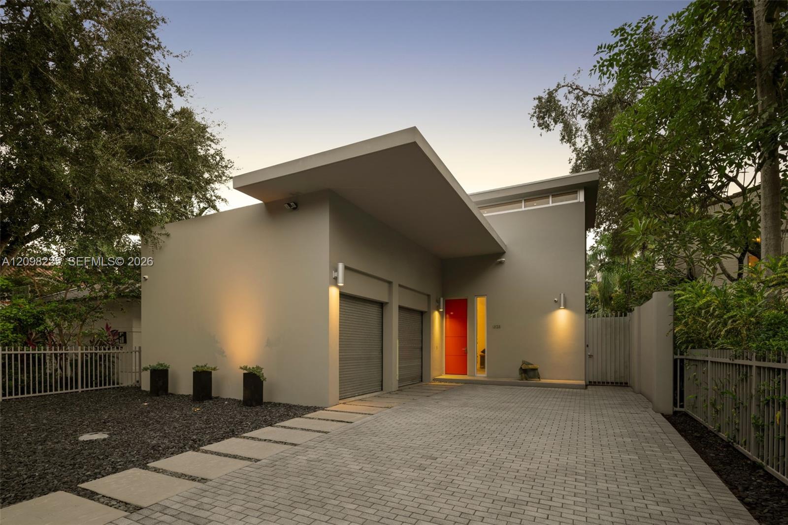 Modern architectural exterior featuring a prominent shed roofline, dual-car garage with roll-up doors, paver driveway, and a solid red entry door
