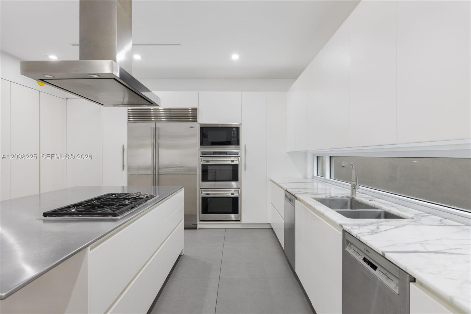 Contemporary kitchen featuring flat-panel cabinetry, stainless steel island countertop with integrated cooktop, stone-surface perimeter countertops, stainless steel wall ovens, and recessed ceiling lighting