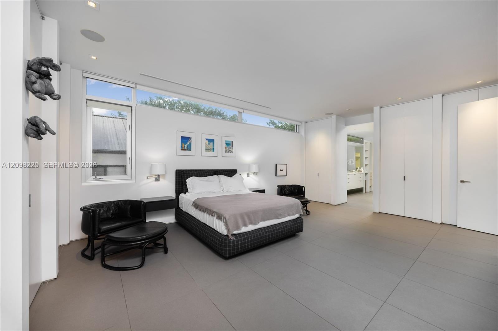 Large-format tile flooring, clerestory windows, recessed ceiling lighting, wall-mounted bedside lamps, and floor-to-ceiling built-in cabinetry
