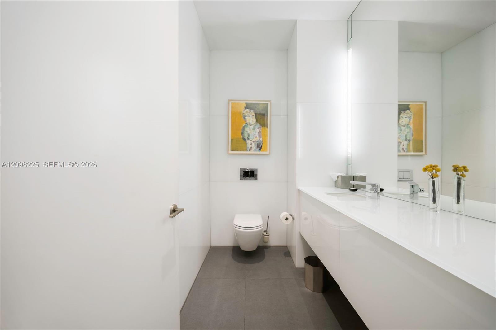 Wall-mounted toilet with a concealed tank, floating vanity with an integrated basin, large-format mirror, and matte-finish grey floor tile