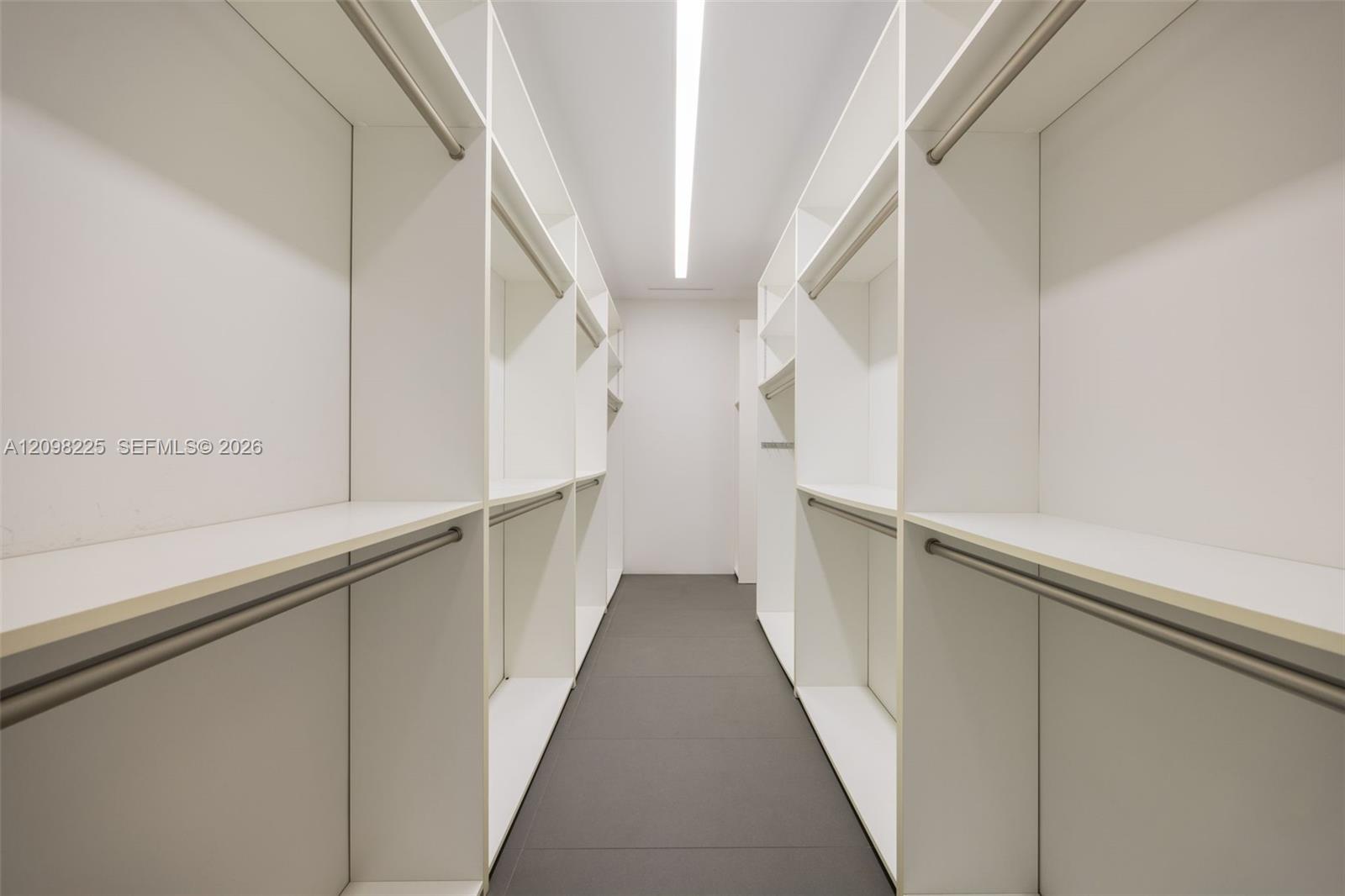 Walk-in closet featuring white built-in shelving, integrated hanging rods, flush-mount linear ceiling lighting, and tile flooring