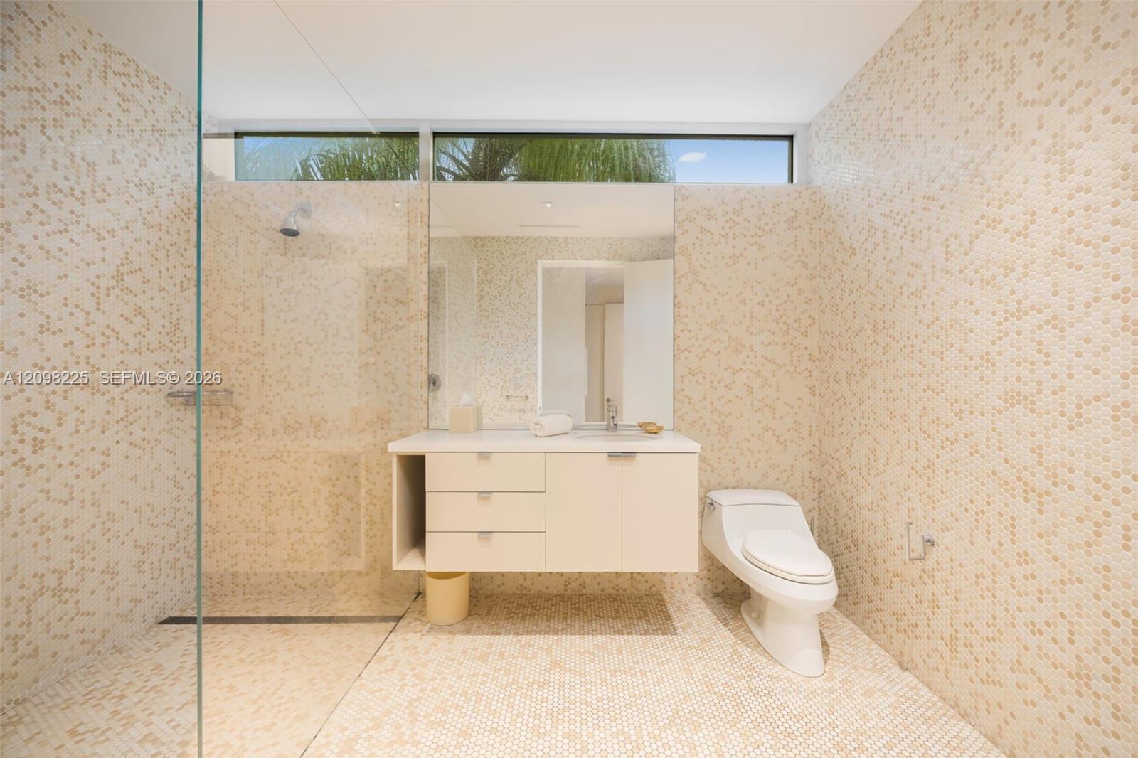 Spa-inspired bathroom featuring a frameless glass shower enclosure, floating vanity with soft-close drawers, large illuminated mirror, and mosaic tile finishes throughout