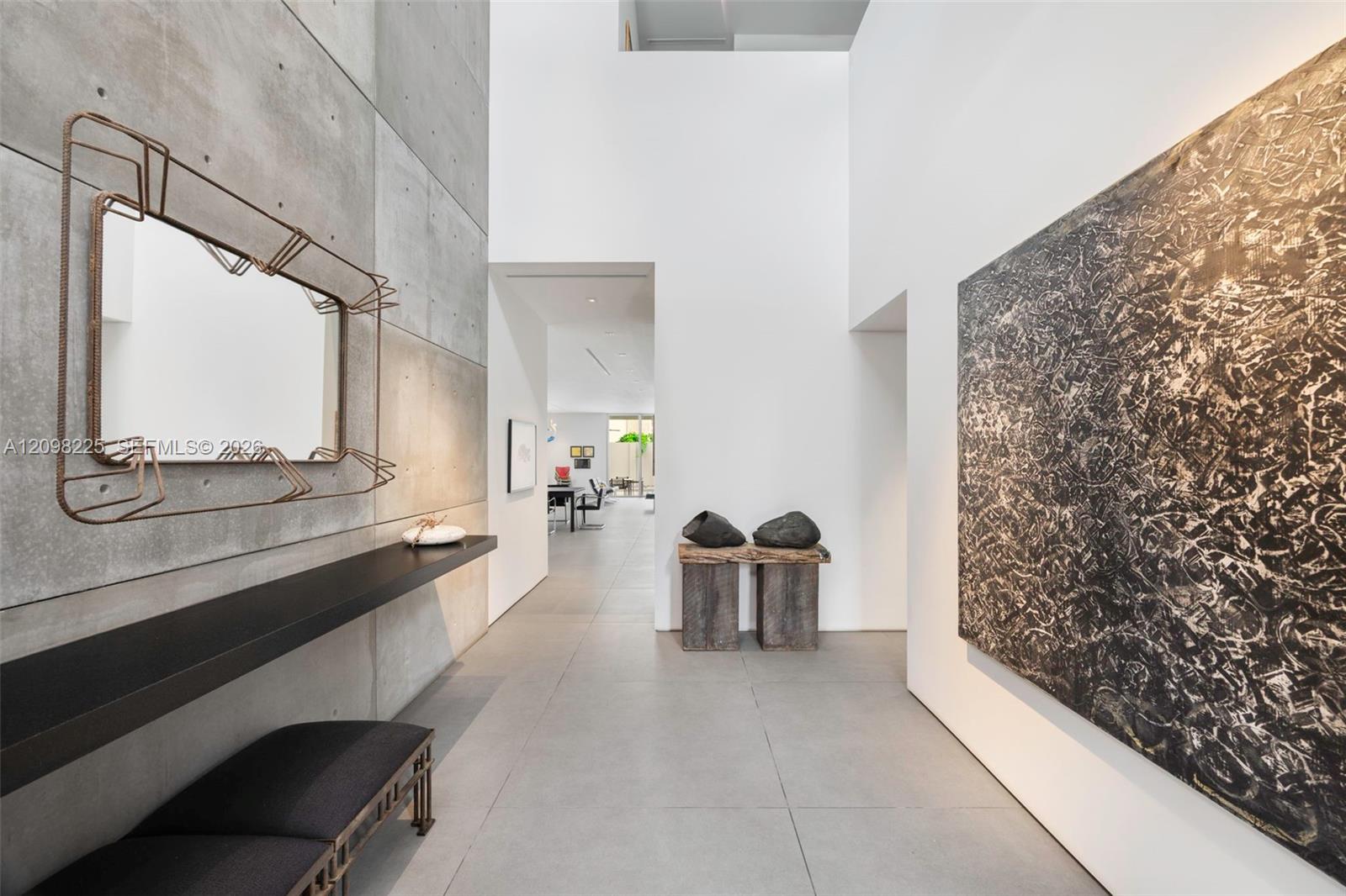 Double-height ceiling featuring exposed concrete paneling, large-format tile flooring, and a minimalist built-in wall-mounted console