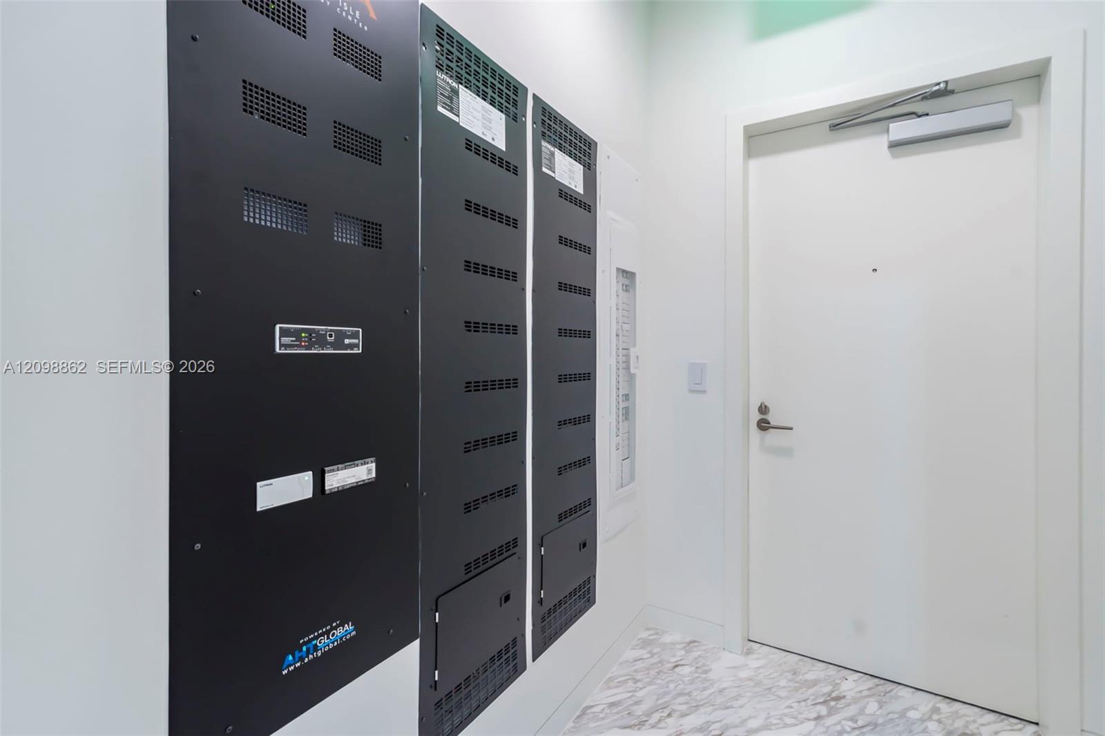 Utility closet featuring integrated technology panels, recessed electrical distribution equipment, and a solid-core door with a hydraulic closure mechanism