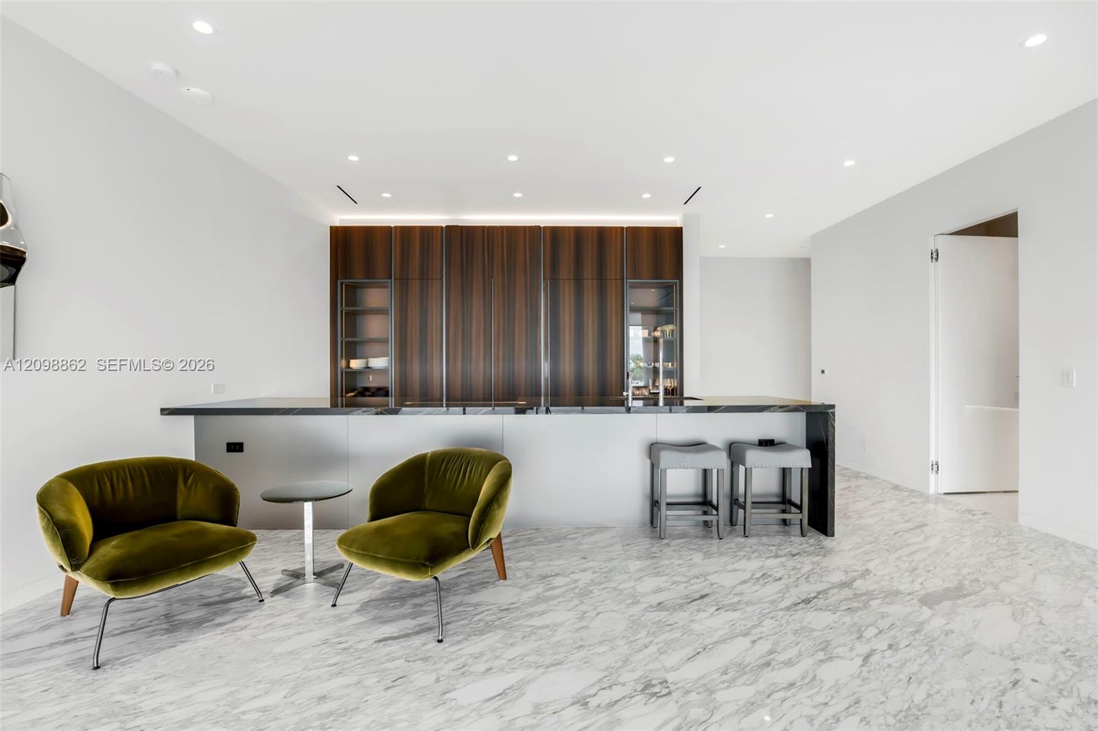 Modern kitchen featuring full-height wood-finish cabinetry, sleek stone-surfaced island, recessed lighting, and continuous stone-patterned flooring Modern kitchen featuring full-height wood-finish cabinetry, sleek stone-surfaced island, recessed lighting, and continuous stone-patterned flooring