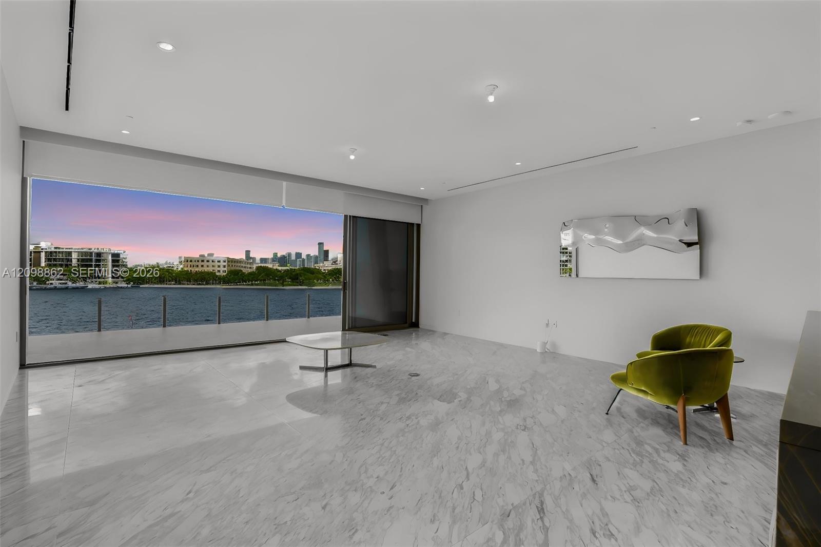 Polished stone flooring, expansive floor-to-ceiling glass sliding doors, recessed ceiling lighting, and a private balcony overlooking the water and urban skyline