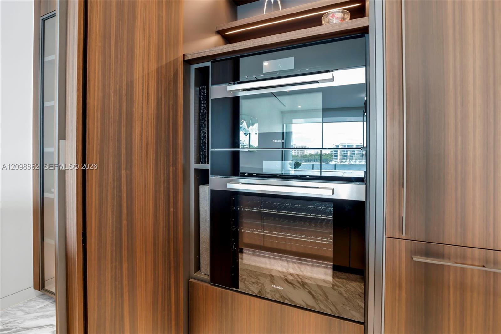 Built-in stainless steel double wall ovens, wood-finish cabinetry, integrated task lighting, and open shelving Built-in stainless steel double wall ovens, wood-finish cabinetry, integrated task lighting, and open shelving