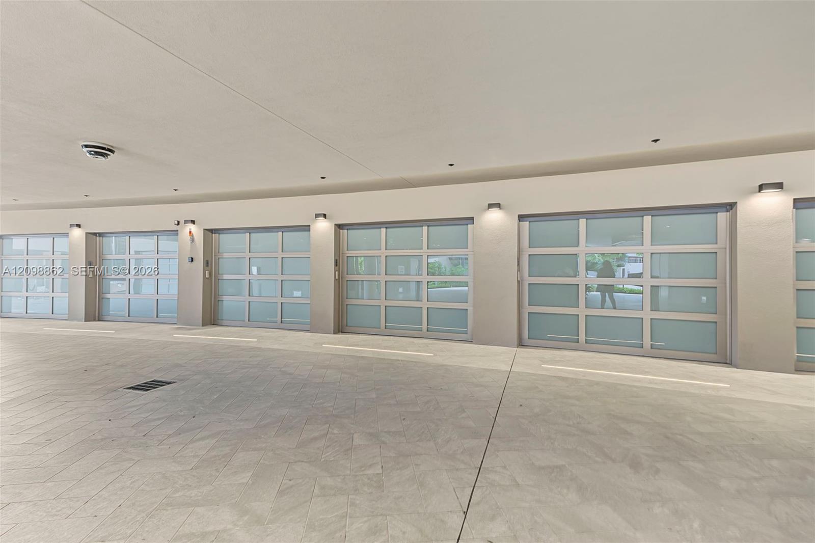 Multi-bay garage featuring frosted glass sectional doors, herringbone-patterned stone flooring, and wall-mounted exterior sconces