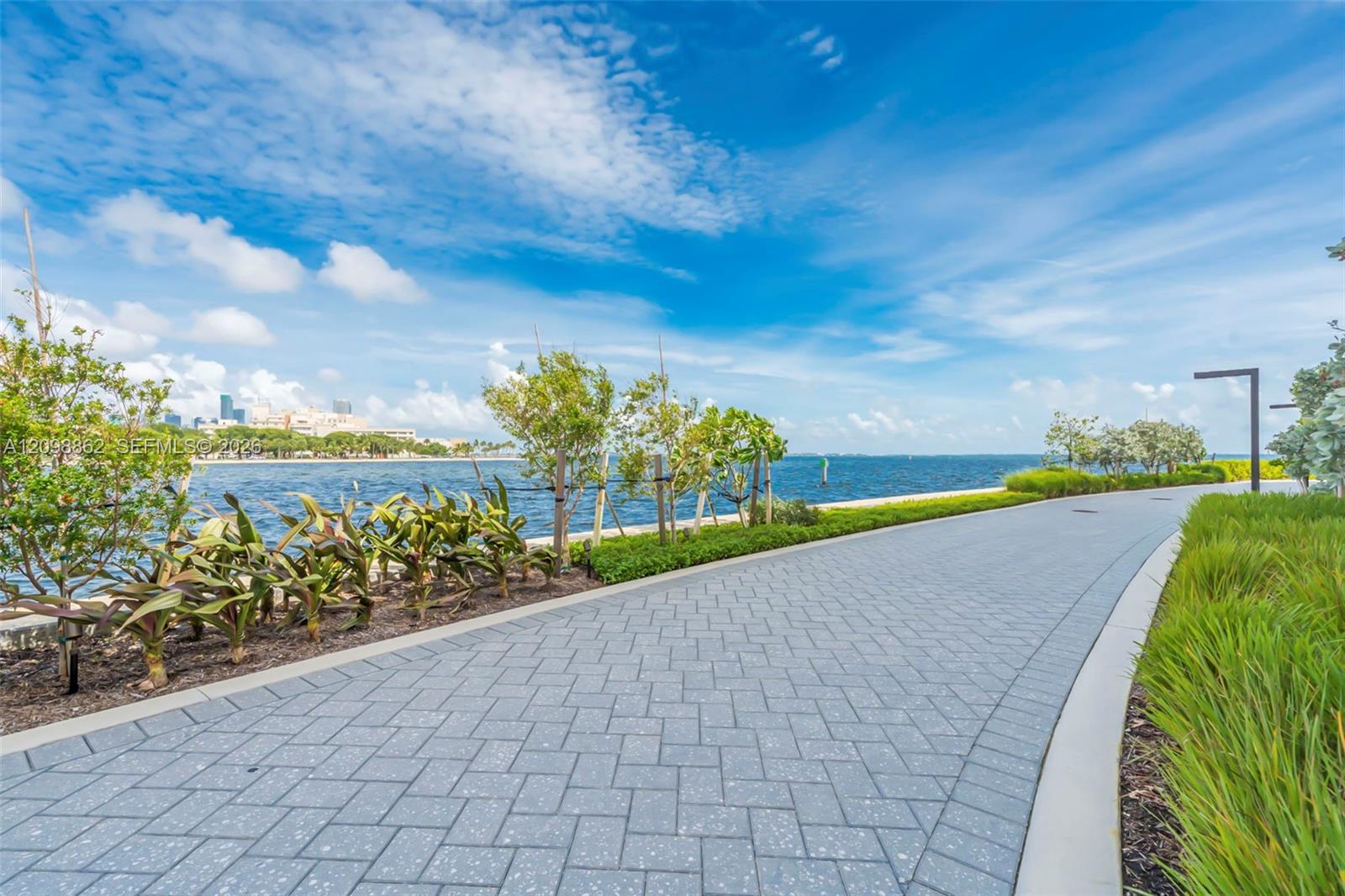 Waterfront paved walkway featuring herringbone patterned pavers, decorative landscaping, and modern pole lighting