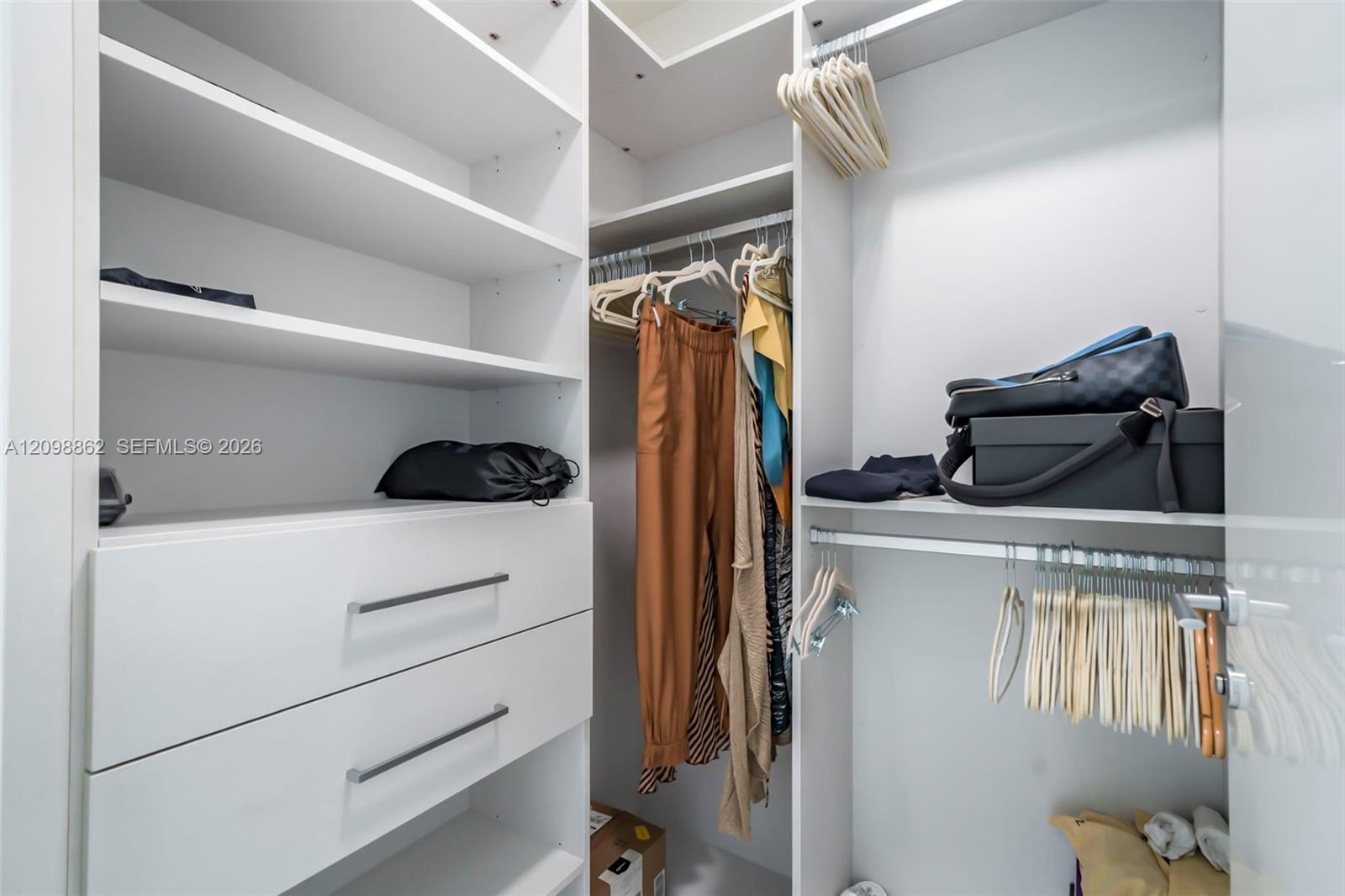 Walk-in closet featuring white built-in cabinetry, dual pull-out drawers with minimalist hardware, adjustable shelving, and multi-level hanging rods