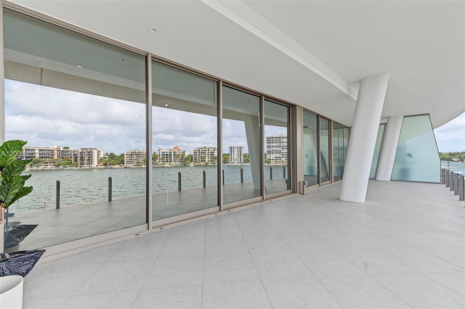 Covered outdoor terrace featuring large-format tile flooring, floor-to-ceiling glass panels, structural architectural columns, and water frontage