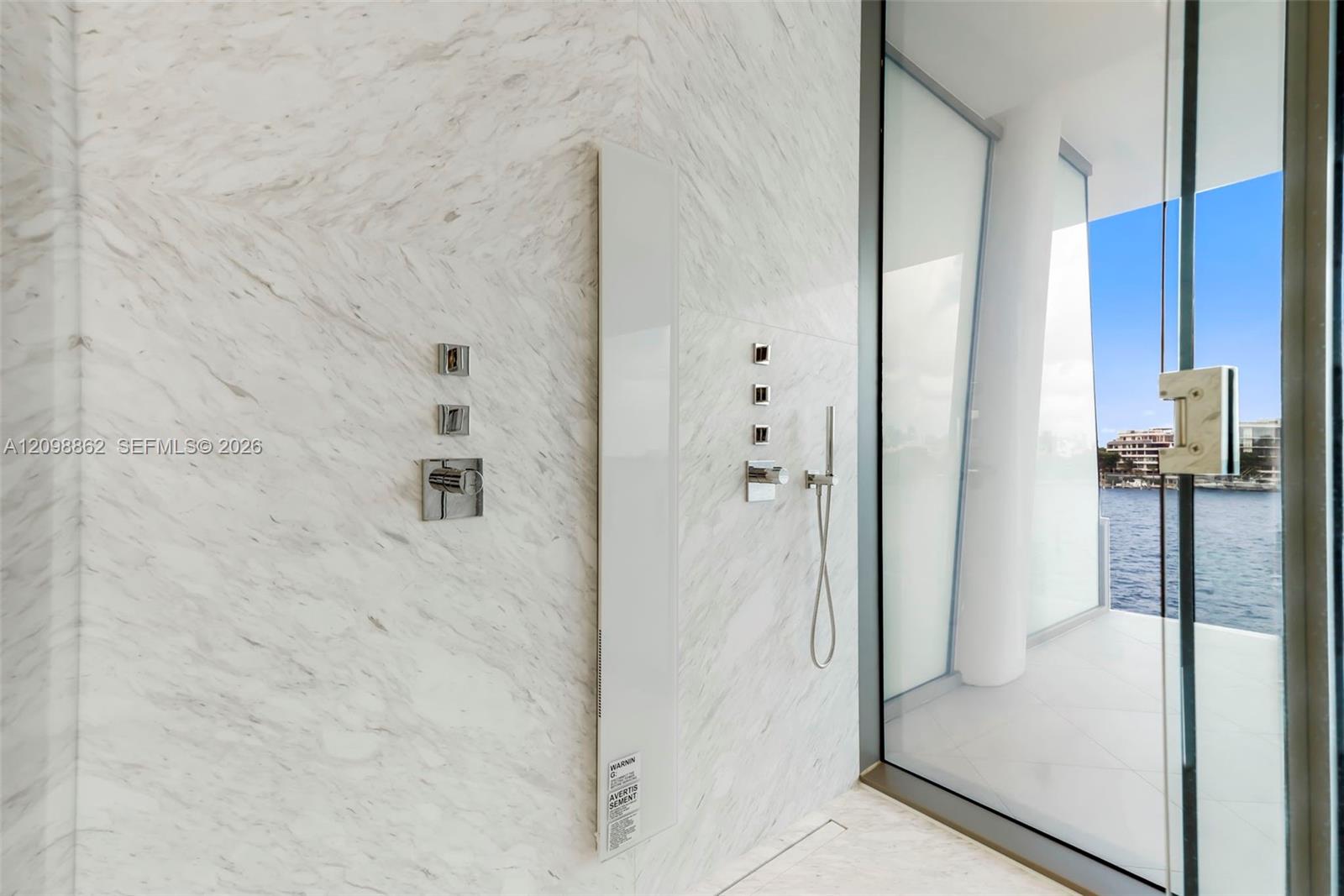 Walk-in shower featuring large-format stone wall tiling, polished chrome wall-mounted fixtures, a minimalist integrated vertical shower panel, and floor-to-ceiling glass paneling with direct water access