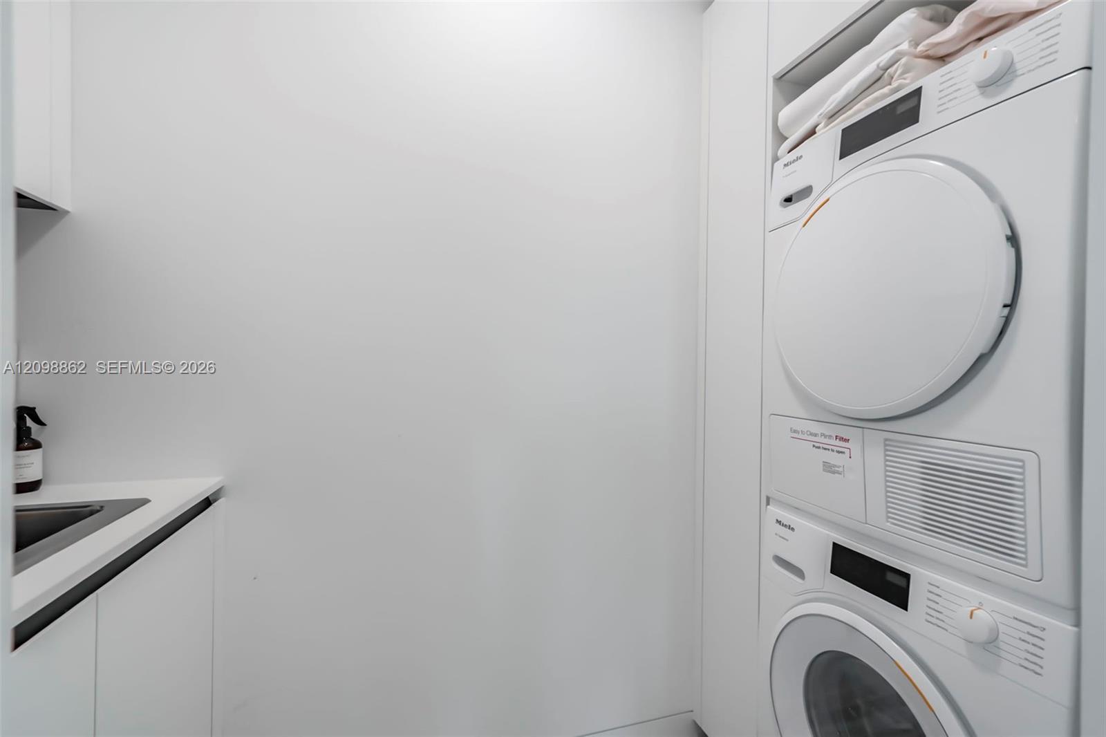 Laundry area featuring stacked white appliances, built-in cabinetry, and a countertop with an integrated sink
