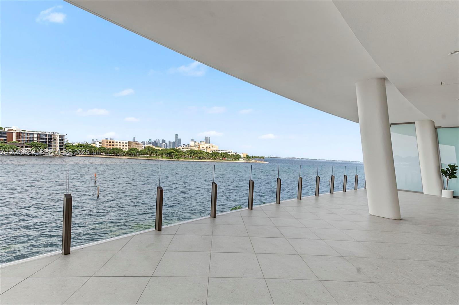 Covered terrace featuring large-format stone tile flooring, structural columns, and a frameless glass railing system