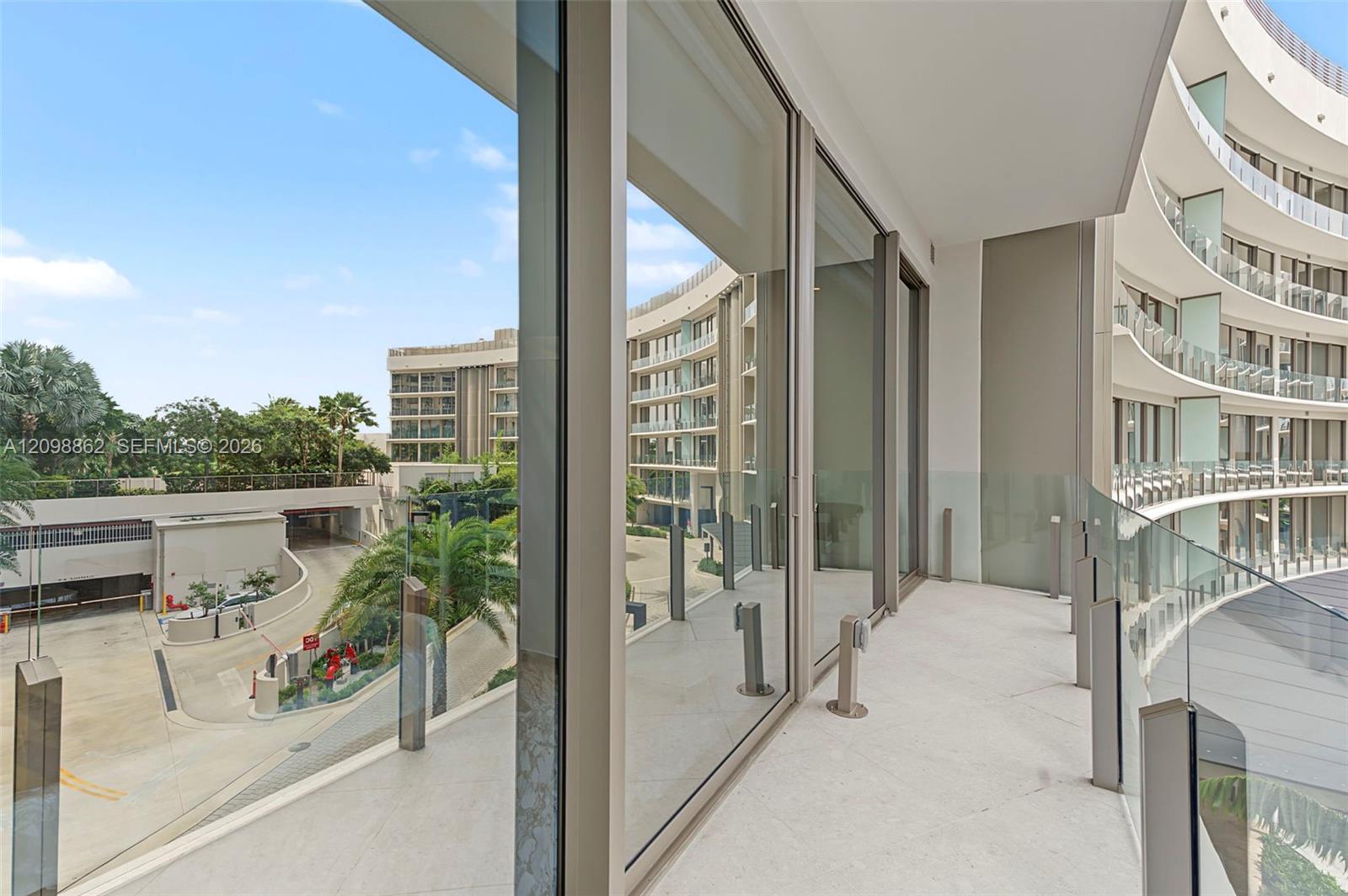 Curved exterior balcony featuring full-height glass sliding doors, stone-tiled flooring, and a glass panel railing