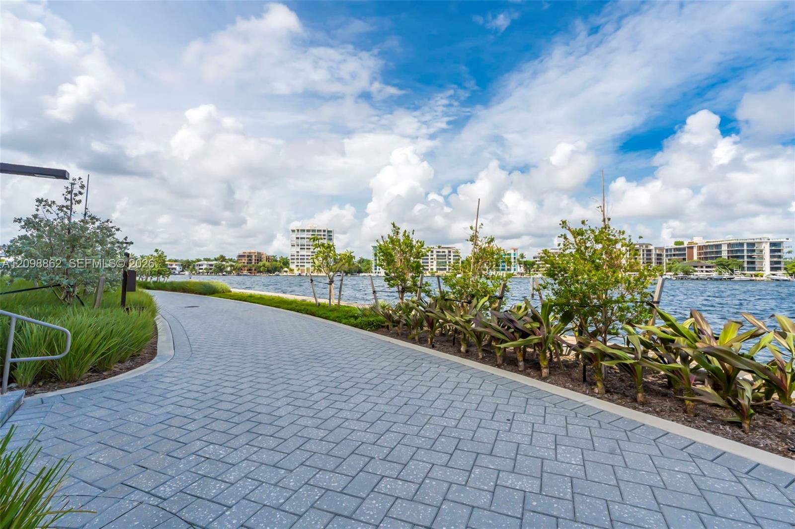 Waterfront walkway featuring concrete paver surfacing, curated tropical landscaping, and metal railing accents