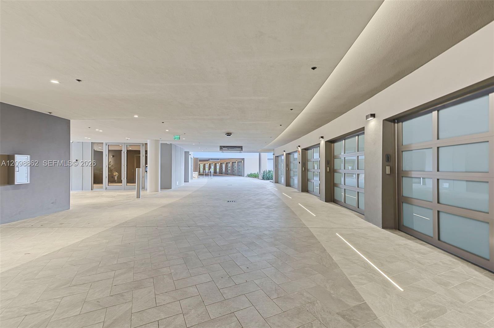 Covered motor court featuring herringbone-patterned stone flooring, tiered LED cove lighting, and multiple garage bays with frosted glass panels