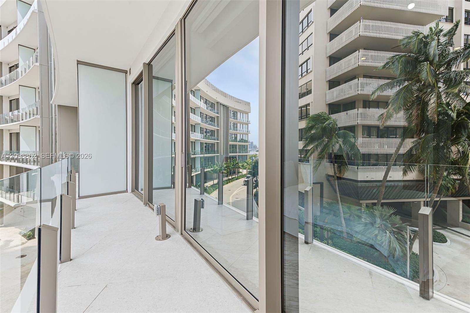 Covered balcony with light-toned flooring, floor-to-ceiling glass panel walls, and a minimalist glass-and-metal railing system