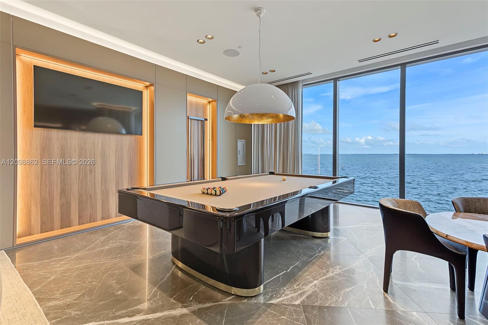 Floor-to-ceiling glass windows, stone flooring, built-in recessed wood-finish wall panels with integrated accent lighting, and a suspended dome pendant light fixture
