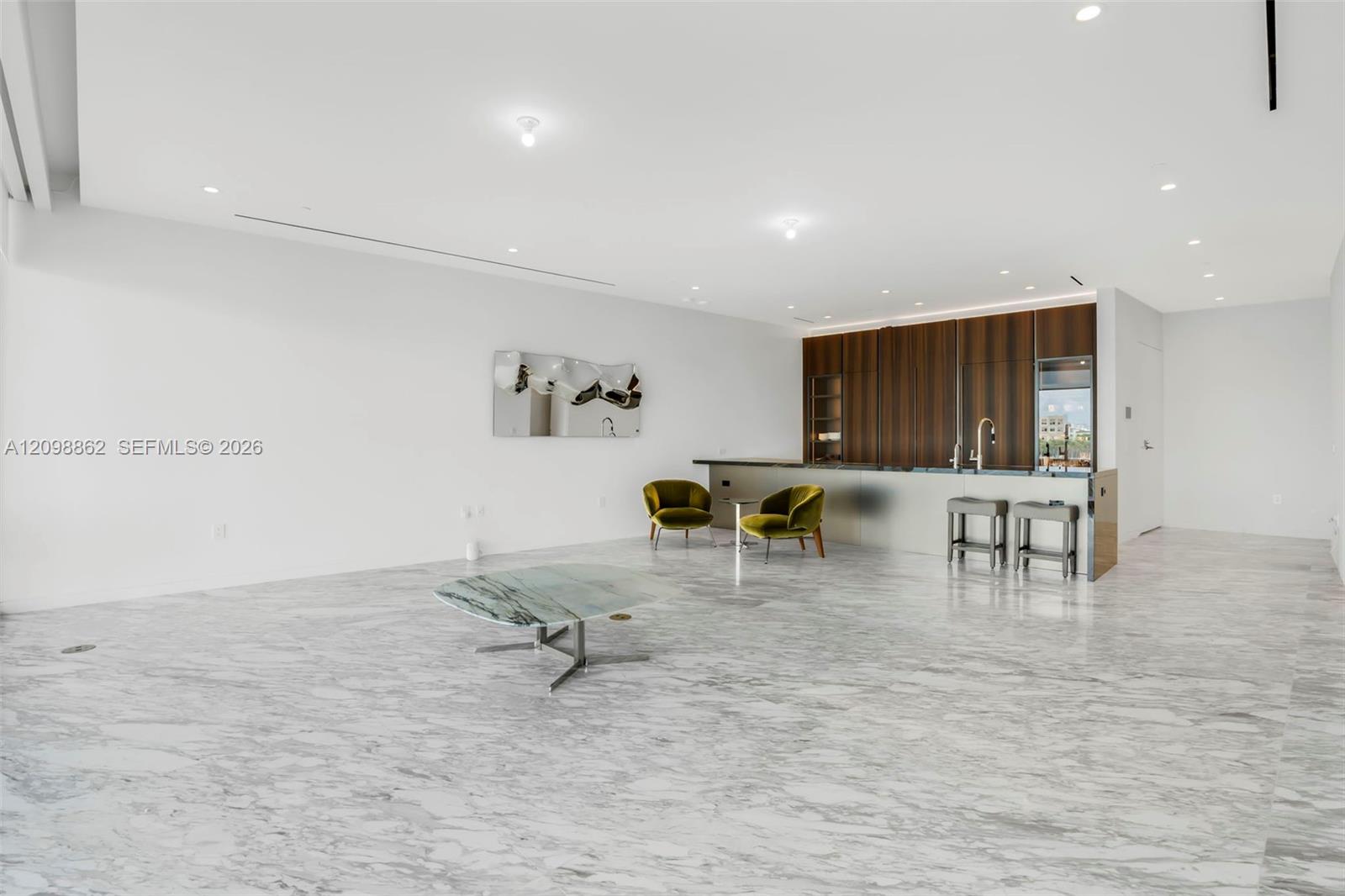 Open-concept interior featuring large-format stone flooring, floor-to-ceiling wood-finish cabinetry, recessed ceiling lighting, and a metallic-finish kitchen island