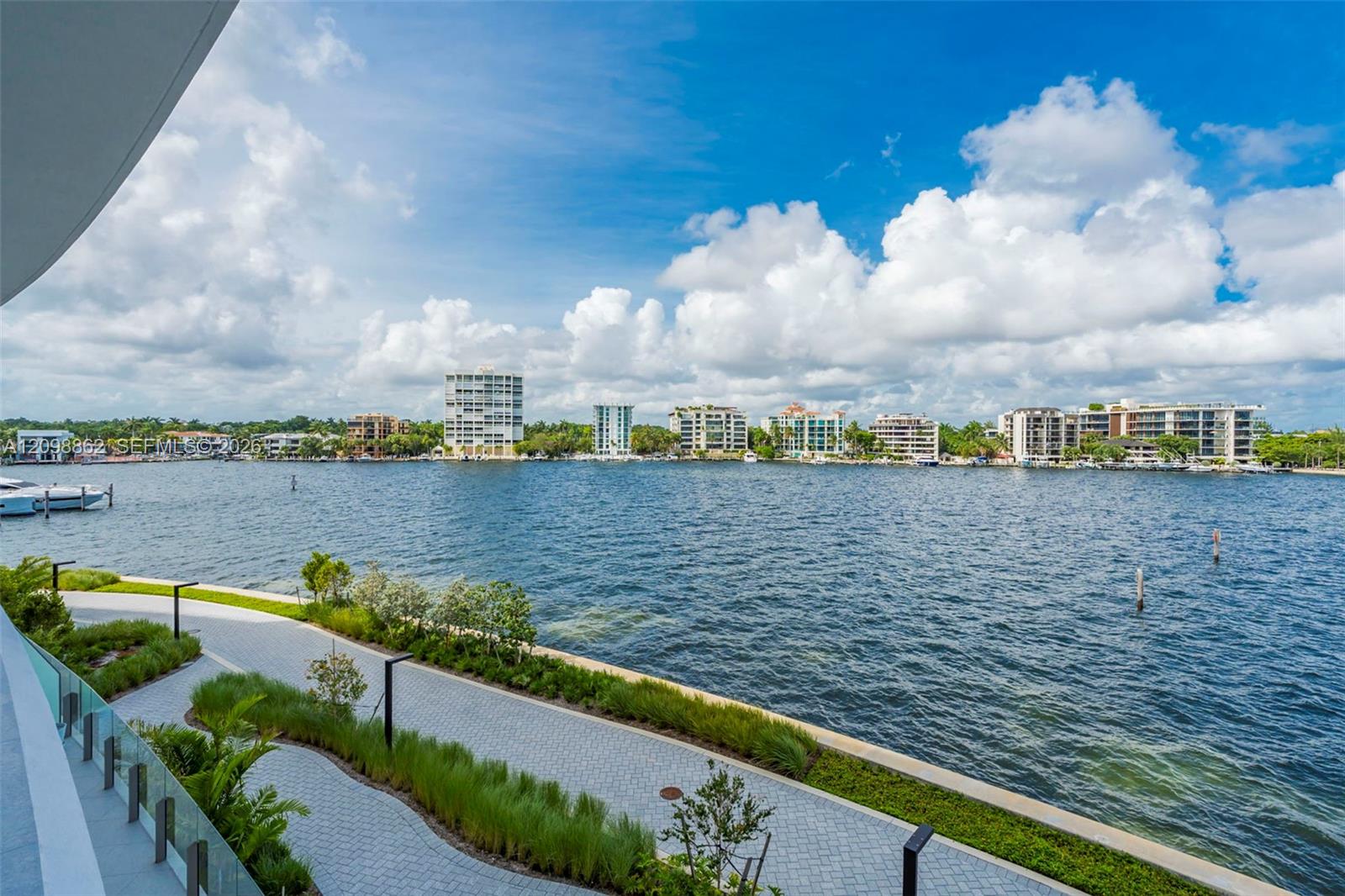 Waterfront terrace with a glass railing, paver walkway, landscaped greenery, and direct water frontage Waterfront terrace with a glass railing, paver walkway, landscaped greenery, and direct water frontage