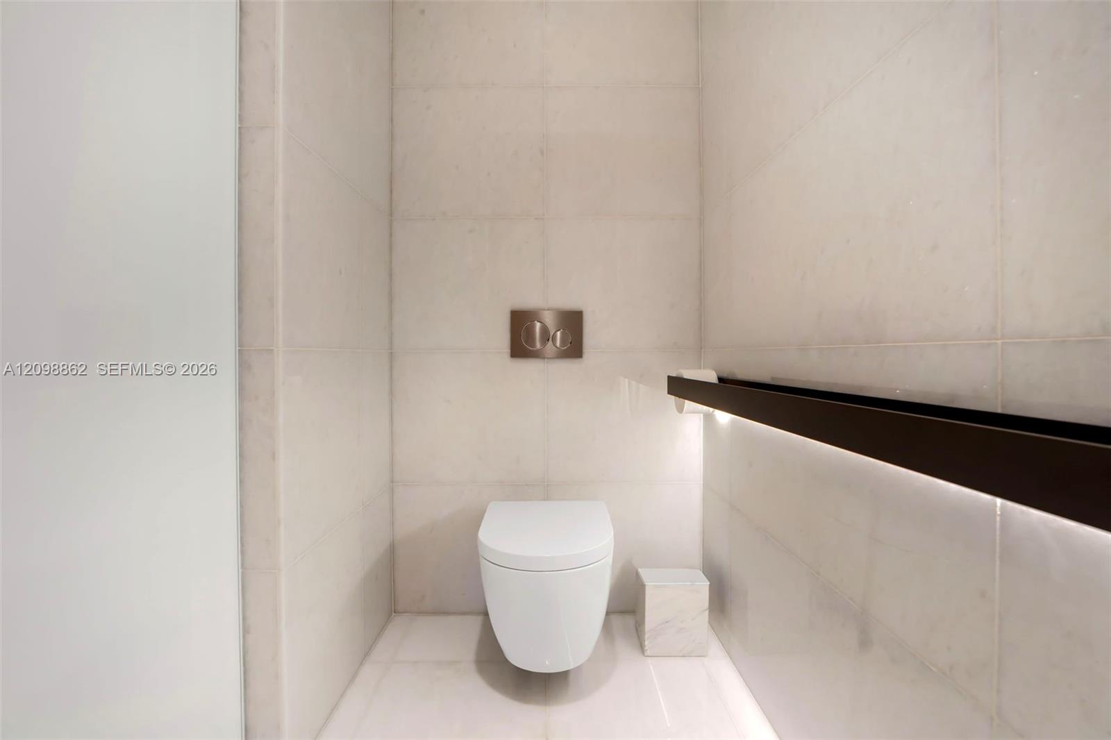 Wall-mounted toilet with a dual-flush actuator plate, floor-to-ceiling large-format tile surround, and integrated linear accent lighting