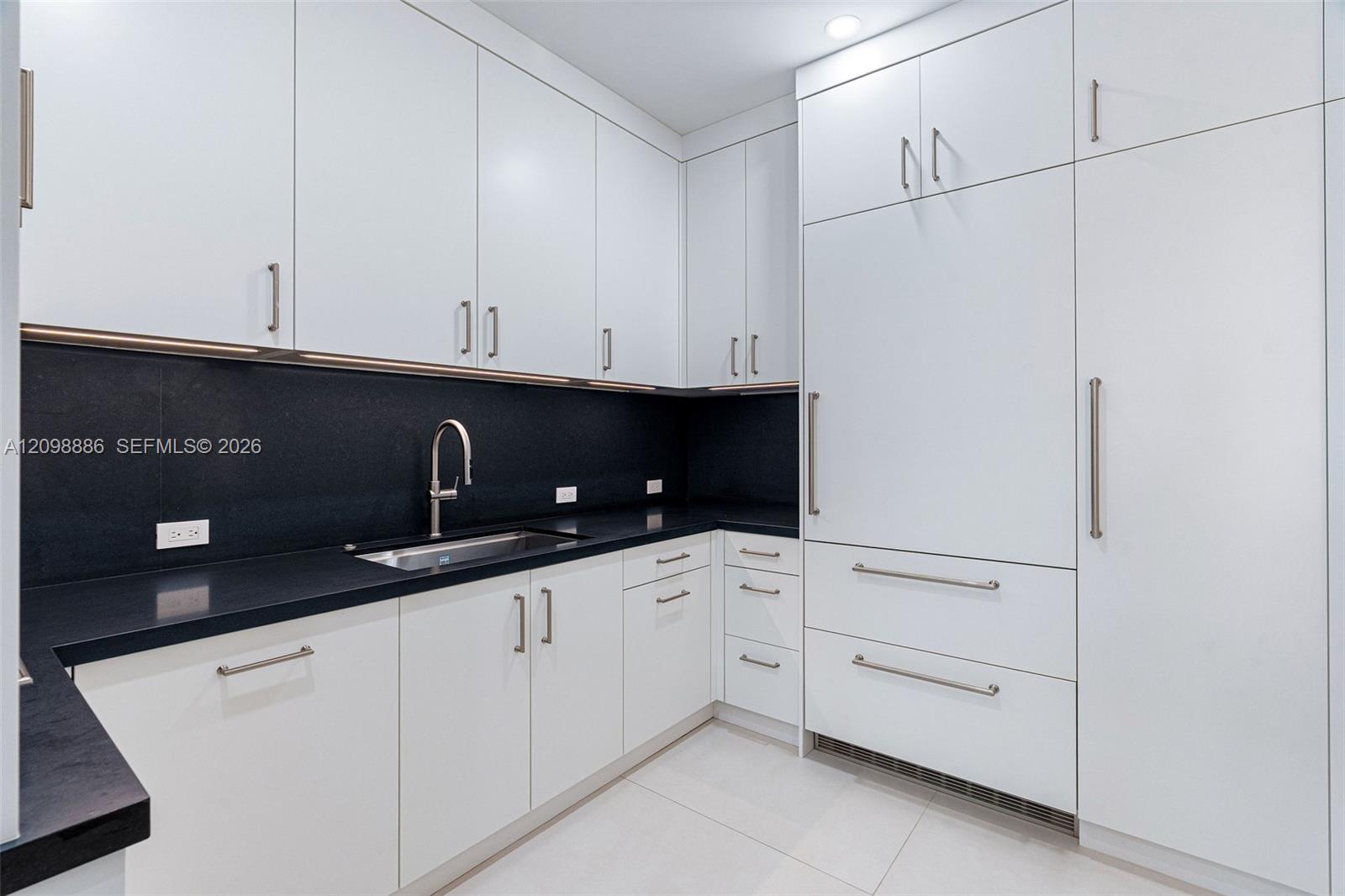 Kitchen featuring flat-panel white cabinetry, contrasting dark stone countertops, integrated panel-ready refrigerator, stainless steel undermount sink with gooseneck faucet, and recessed ceiling lighting
