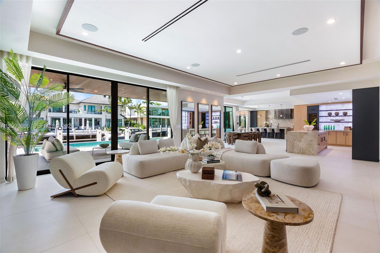 Open-concept living area featuring large-format tile flooring, a recessed tray ceiling with integrated lighting, expansive floor-to-ceiling glass sliding doors, and a gourmet kitchen equipped with stone-surfaced islands and professional-grade cabinetry