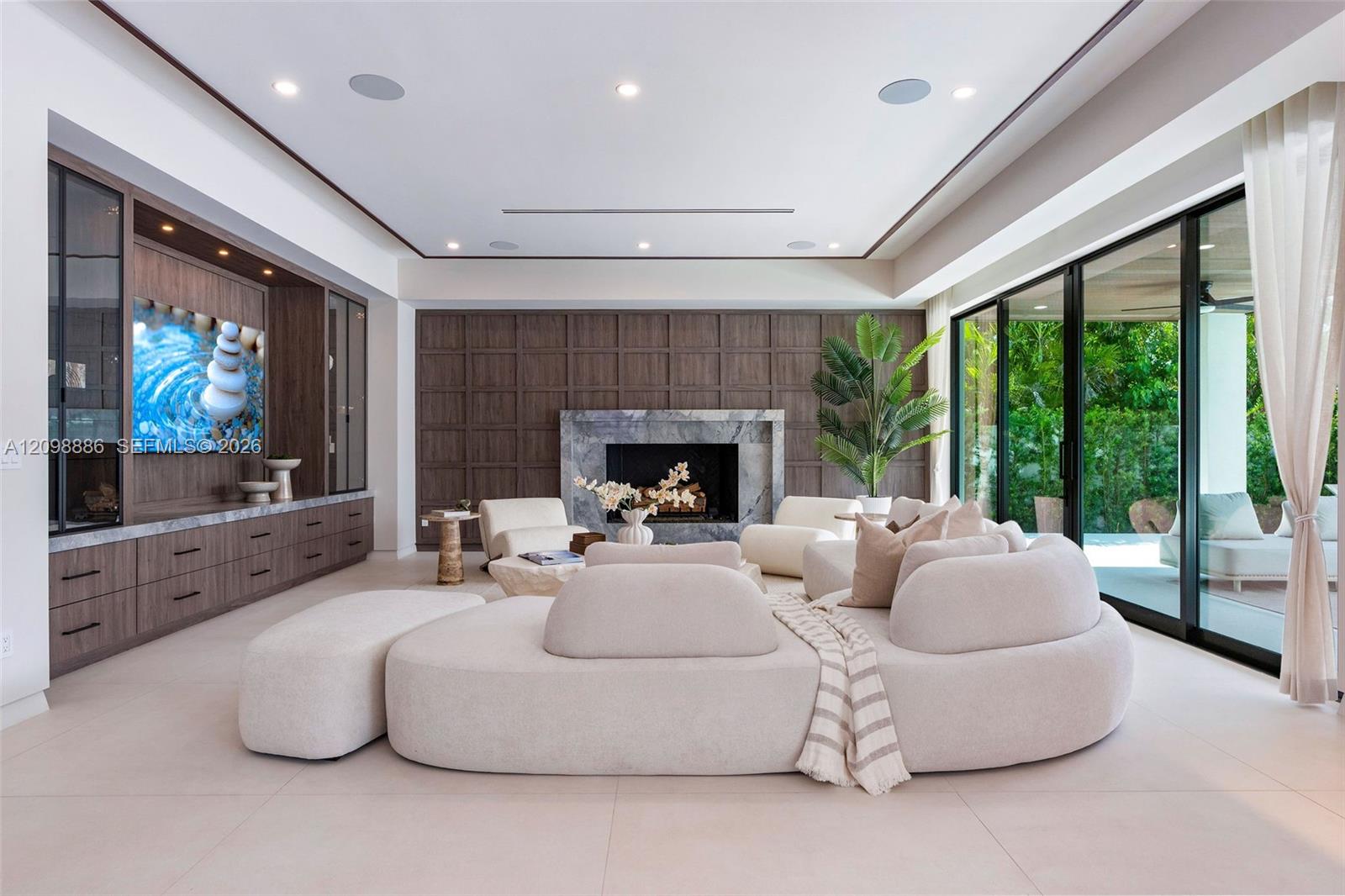 Living area featuring custom wood-finish built-in cabinetry, stone-surround fireplace, dark wood paneled accent wall, recessed ceiling lighting, and floor-to-ceiling sliding glass doors