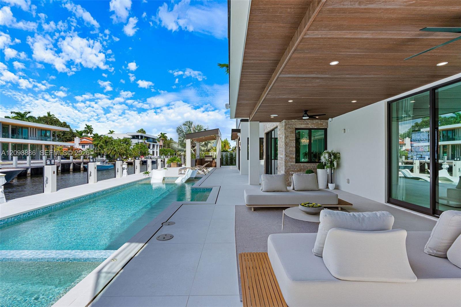 Covered patio featuring a wood-plank ceiling with recessed lighting, integrated lap pool with tiled interior, stacked stone wall accent, and expansive floor-to-ceiling glass sliding doors