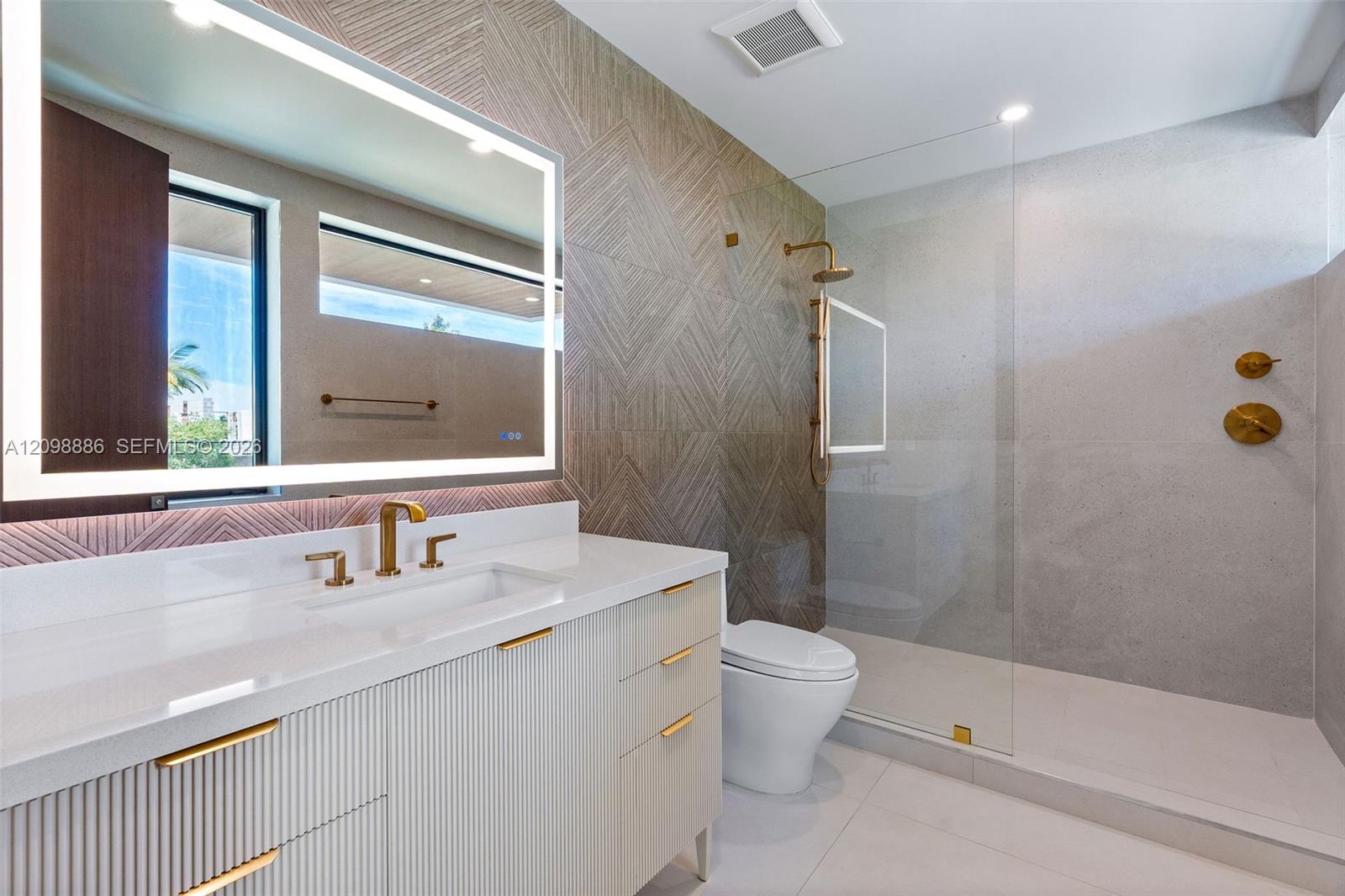 Floating vanity with ribbed cabinetry, solid surface countertop, integrated LED-backlit mirror, and brass-tone fixtures