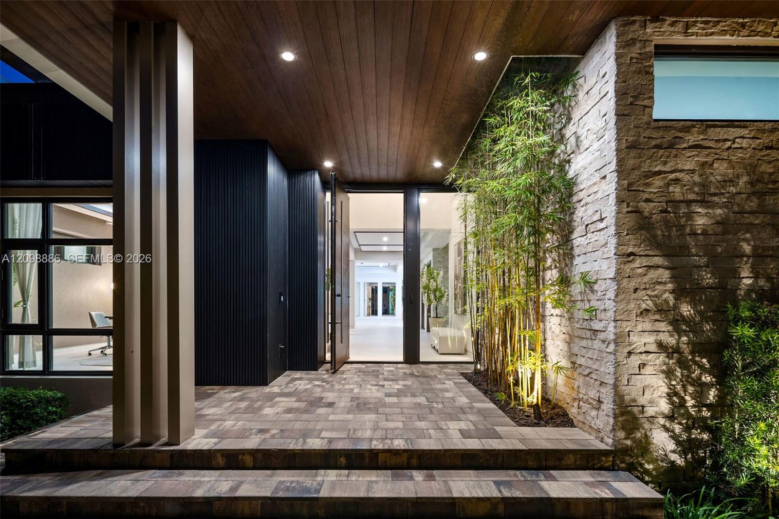 Covered entryway featuring a wood-panelled ceiling, stacked stone accent wall, multi-tiered stone paver stairs, vertical column detailing, and recessed lighting